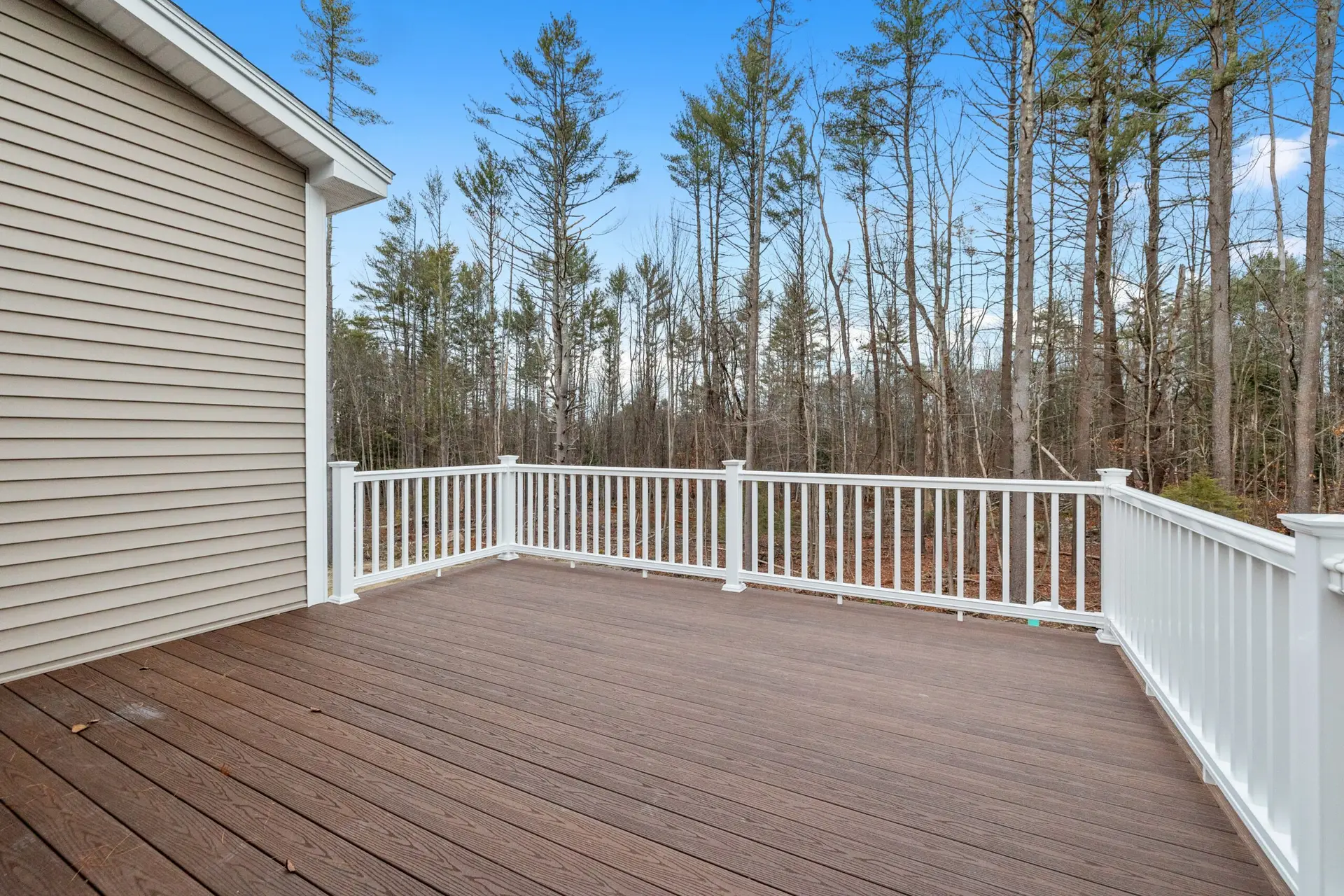 Decking boards of a porch with white railings overlooking a wooded area, showcasing craftsmanship for custom decks in New Hampshire.